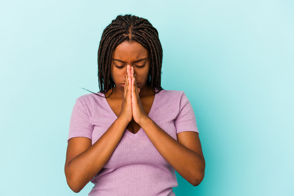 Young african american woman isolated on blue background  praying, showing devotion, religious person looking for divine inspiration.